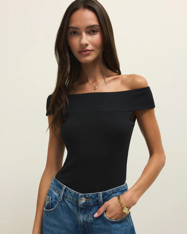 Woman wearing a black off-shoulder top and blue jeans against a plain background