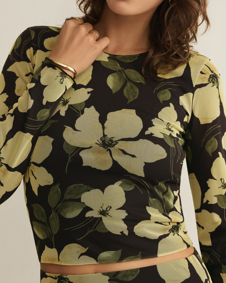 Woman wearing a black dress with large yellow floral patterns on a plain background