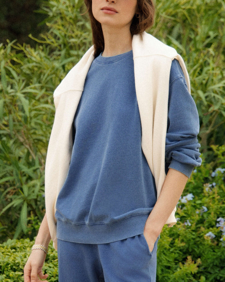 Woman wearing a blue outfit with a white cardigan in a natural setting