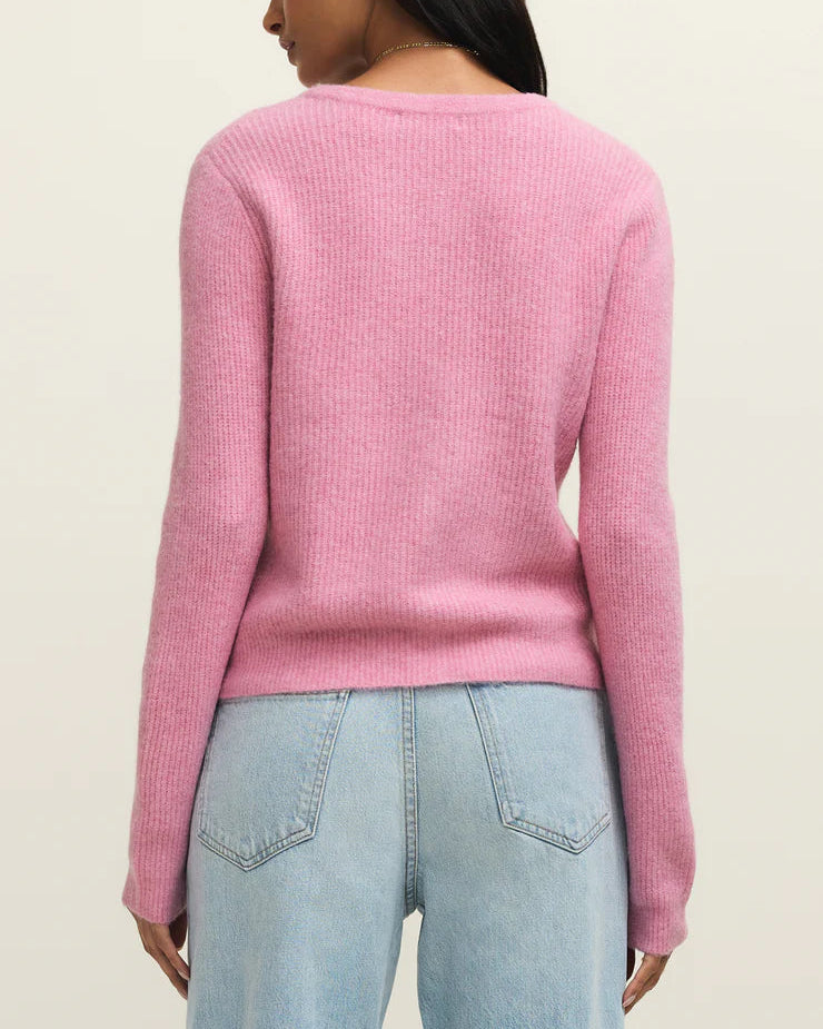 Person wearing a pink sweater and light blue jeans on a beige background
