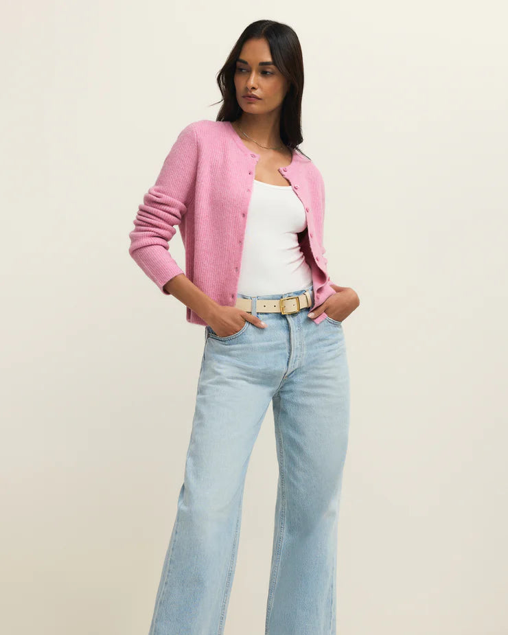 Woman wearing a pink cardigan, white top, light blue jeans, and beige shoes on a plain background