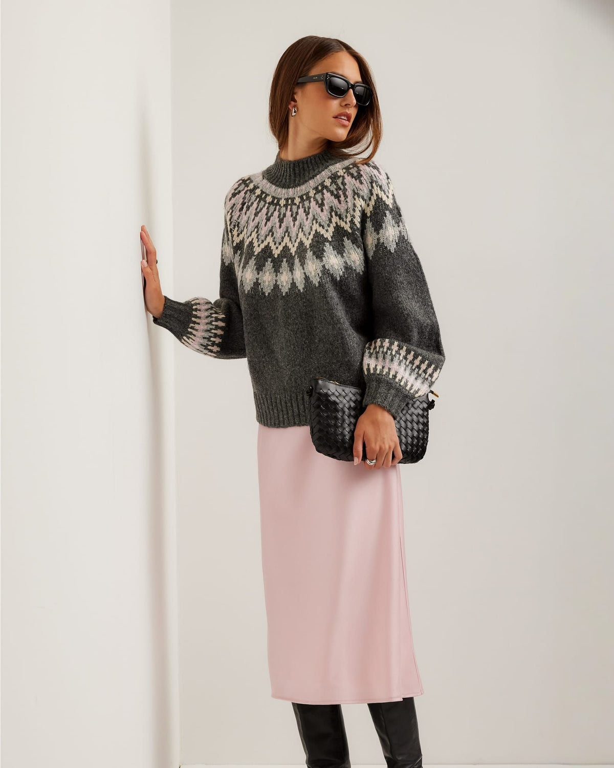 Woman wearing a patterned sweater and pink skirt against a white background