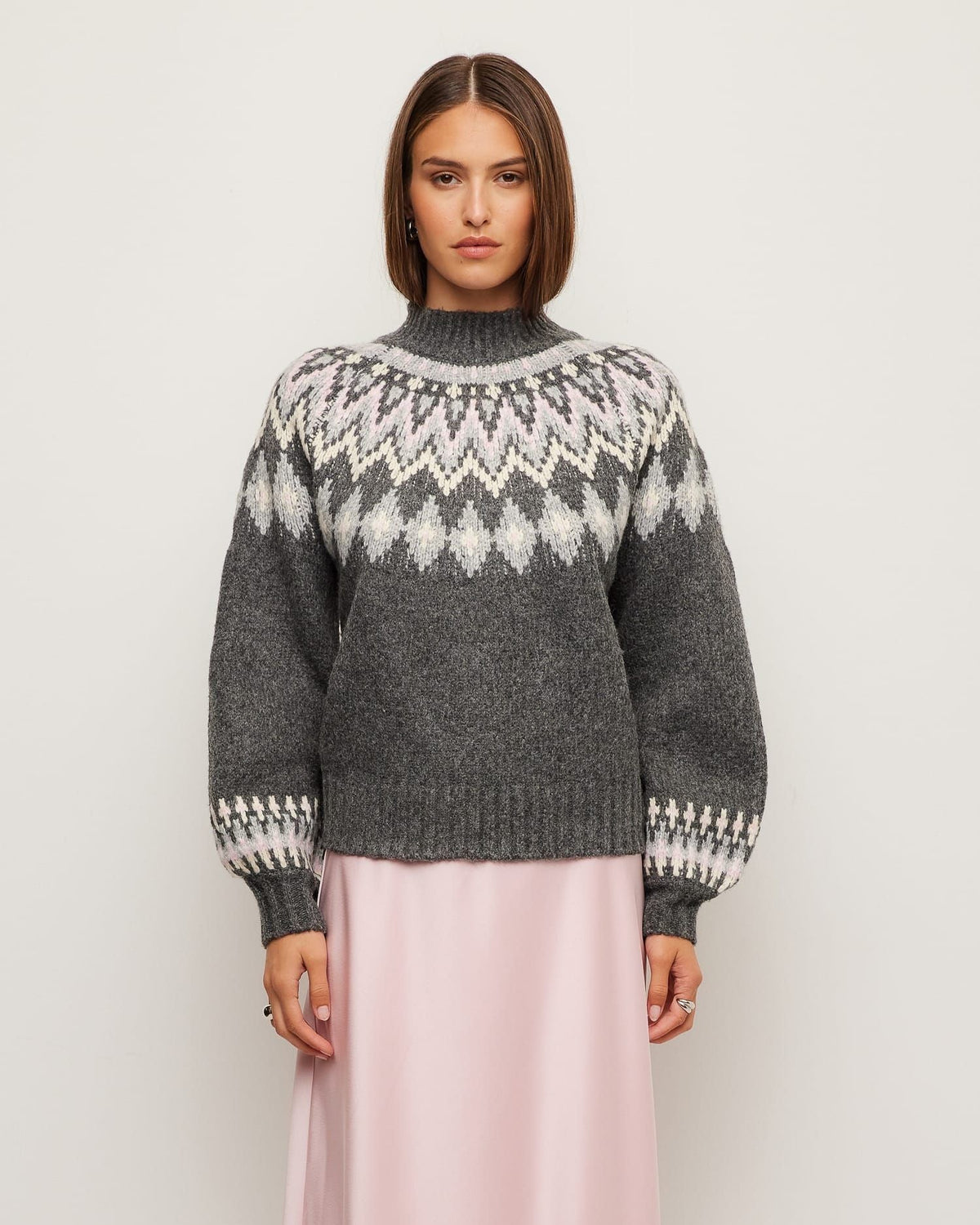 Woman wearing a gray sweater with a patterned design on a plain background
