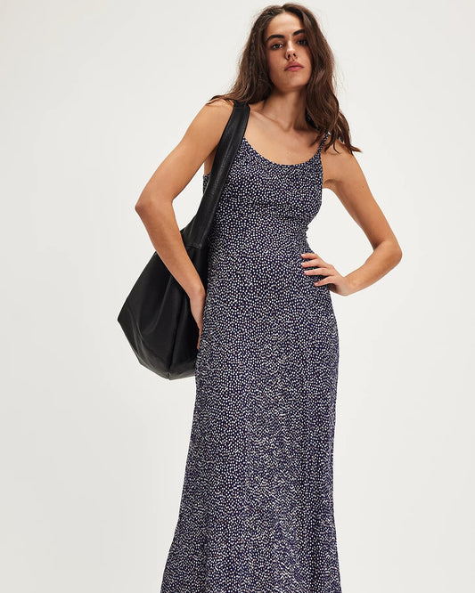 Woman wearing a long patterned dress holding a black bag on a white background