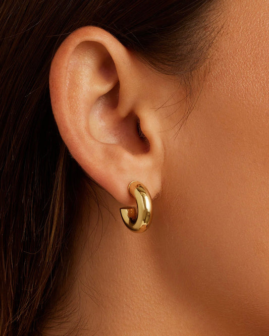 Close up of the Gorjana Lou Statement huggies in gold worn by a model with brown hair.