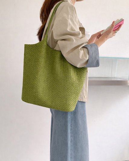 Person holding a green textured tote bag with a plain background