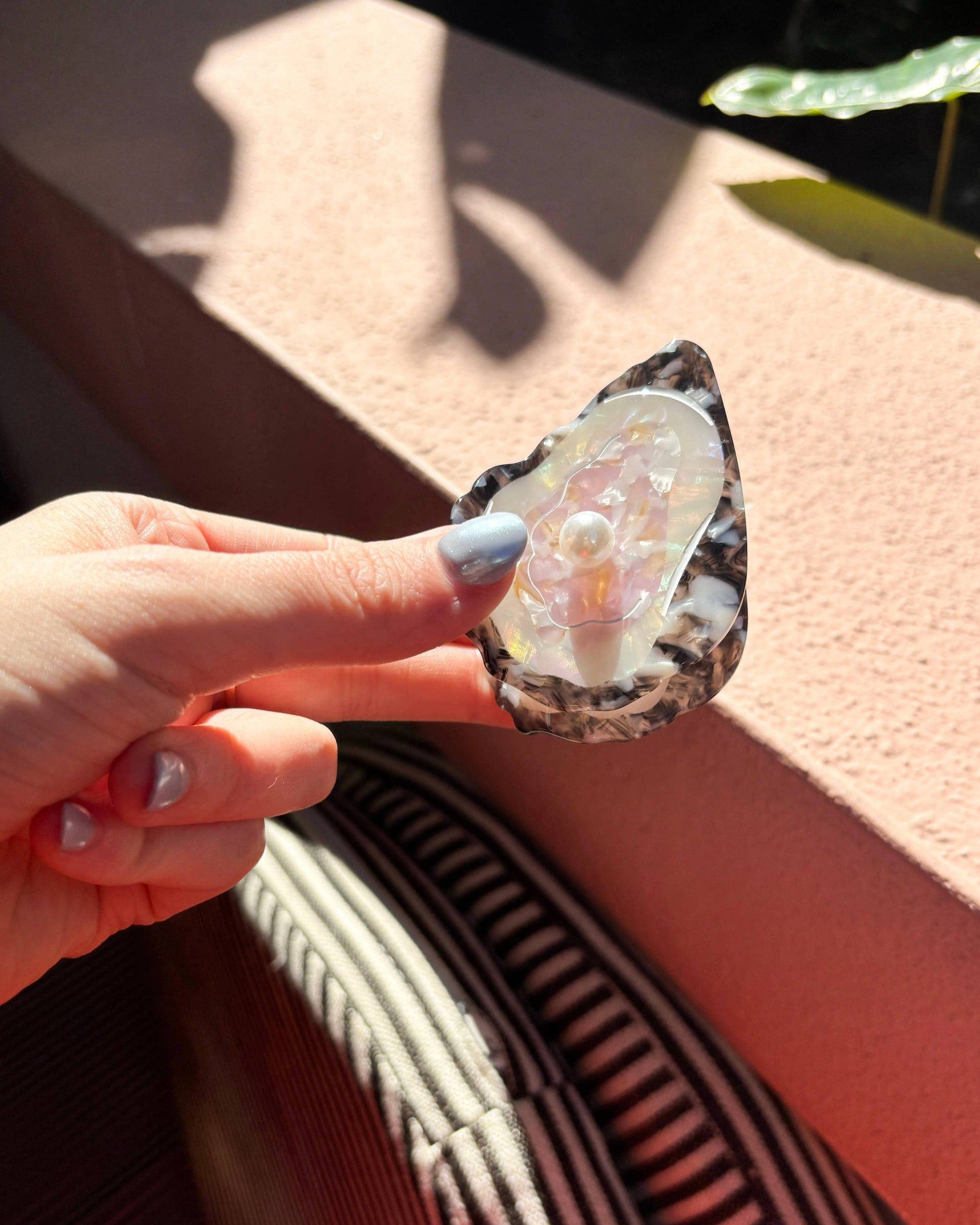 Hand holding an oyster hair clip with a colorful exterior against a neutral background