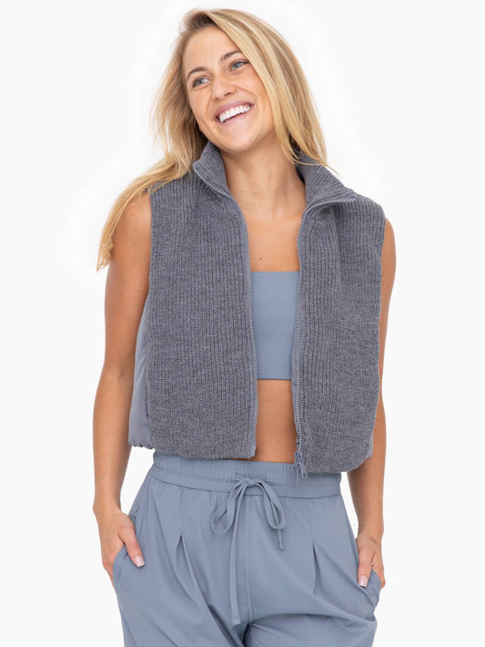 Model wearing Mono B Hybrid Cropped Puffer Vest wearing grey pants and grey tank top on a white background