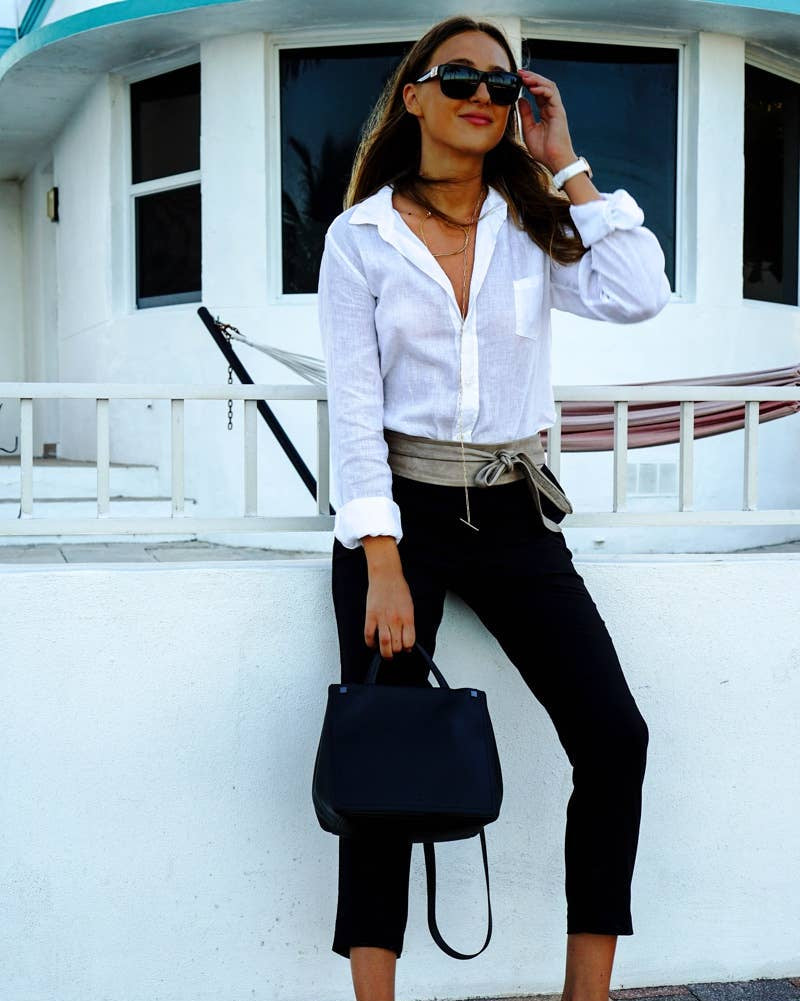 Woman in white shirt and black pants standing on a deck with a white building in the background
