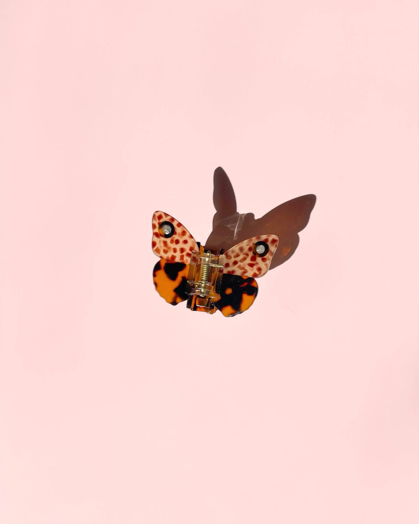 Butterfly-shaped hair clip with leopard print design on a pink background