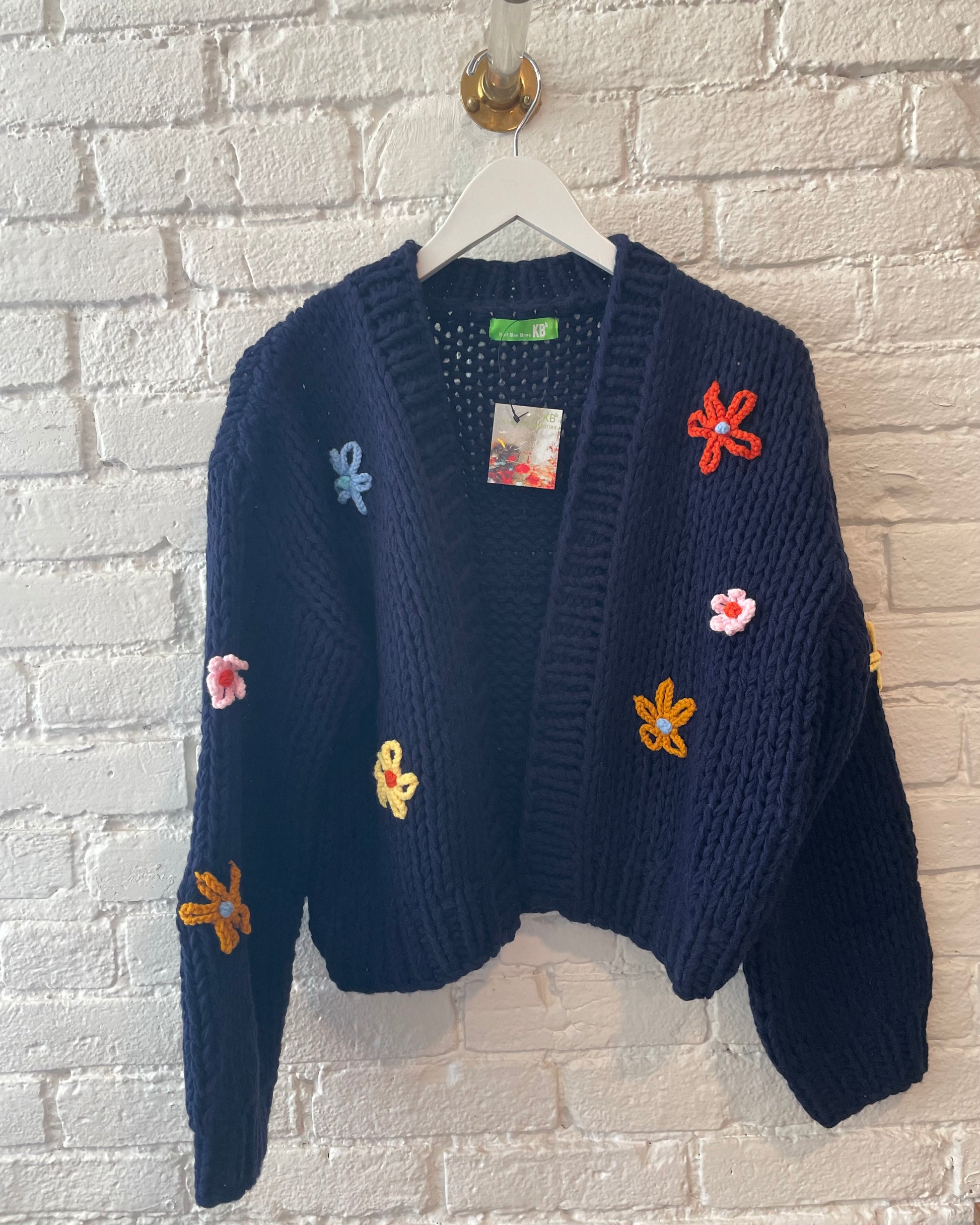 Knit Bon Bons Navy Sweater with multicolored flowers hanging on a white hanger with a white background