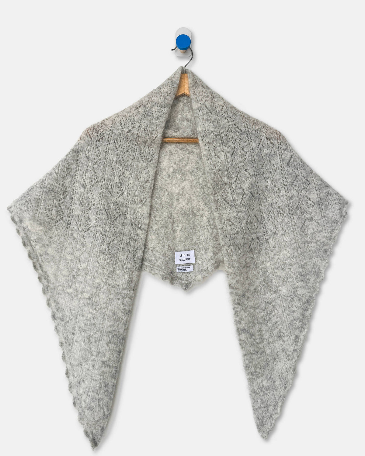 A light gray textured knit shawl draped over a wooden hanger with a blue hook, shown against a plain light gray background.