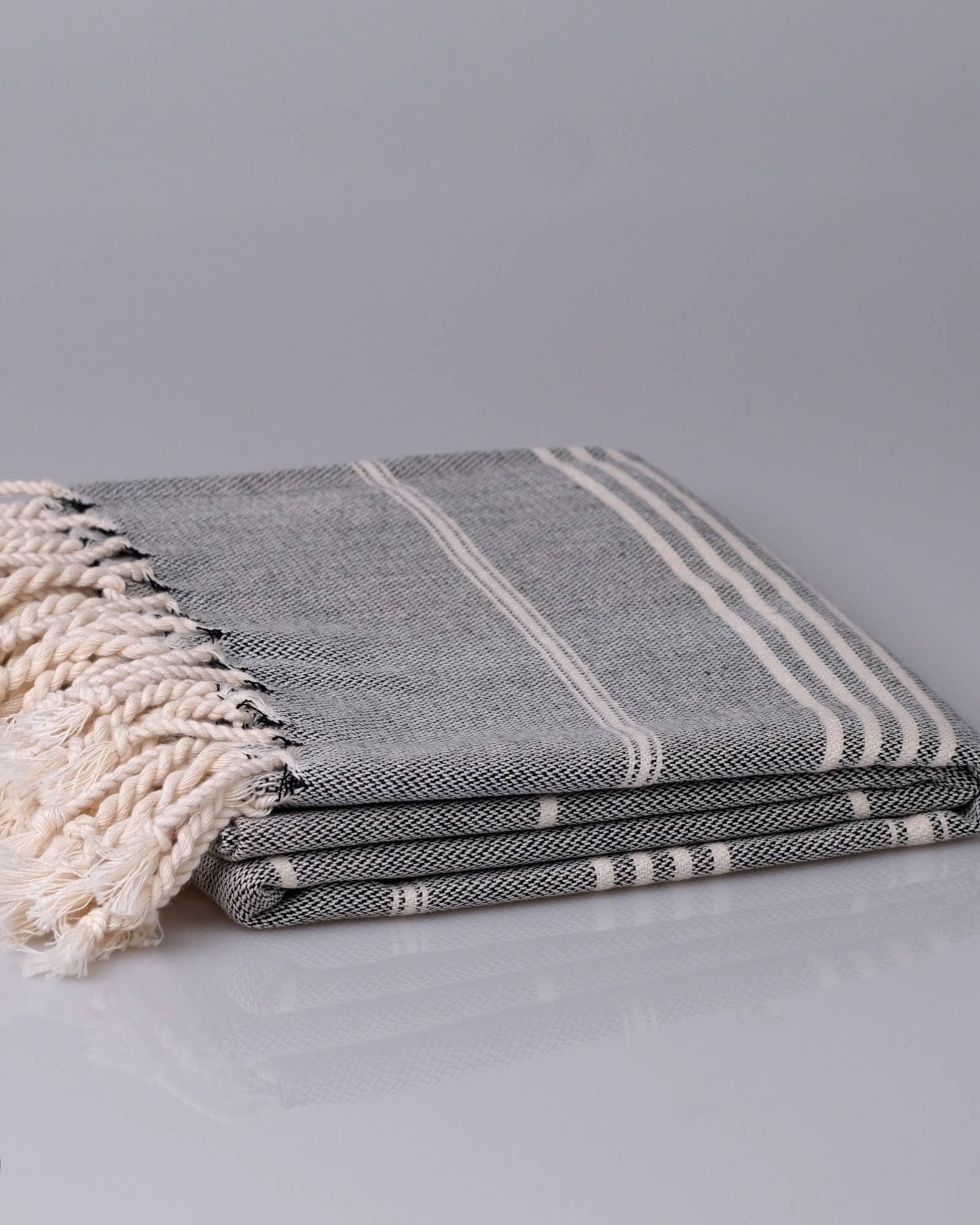 Stack of gray and white striped towels with tassels on a light gray background, featuring the Kalliston brand logo.