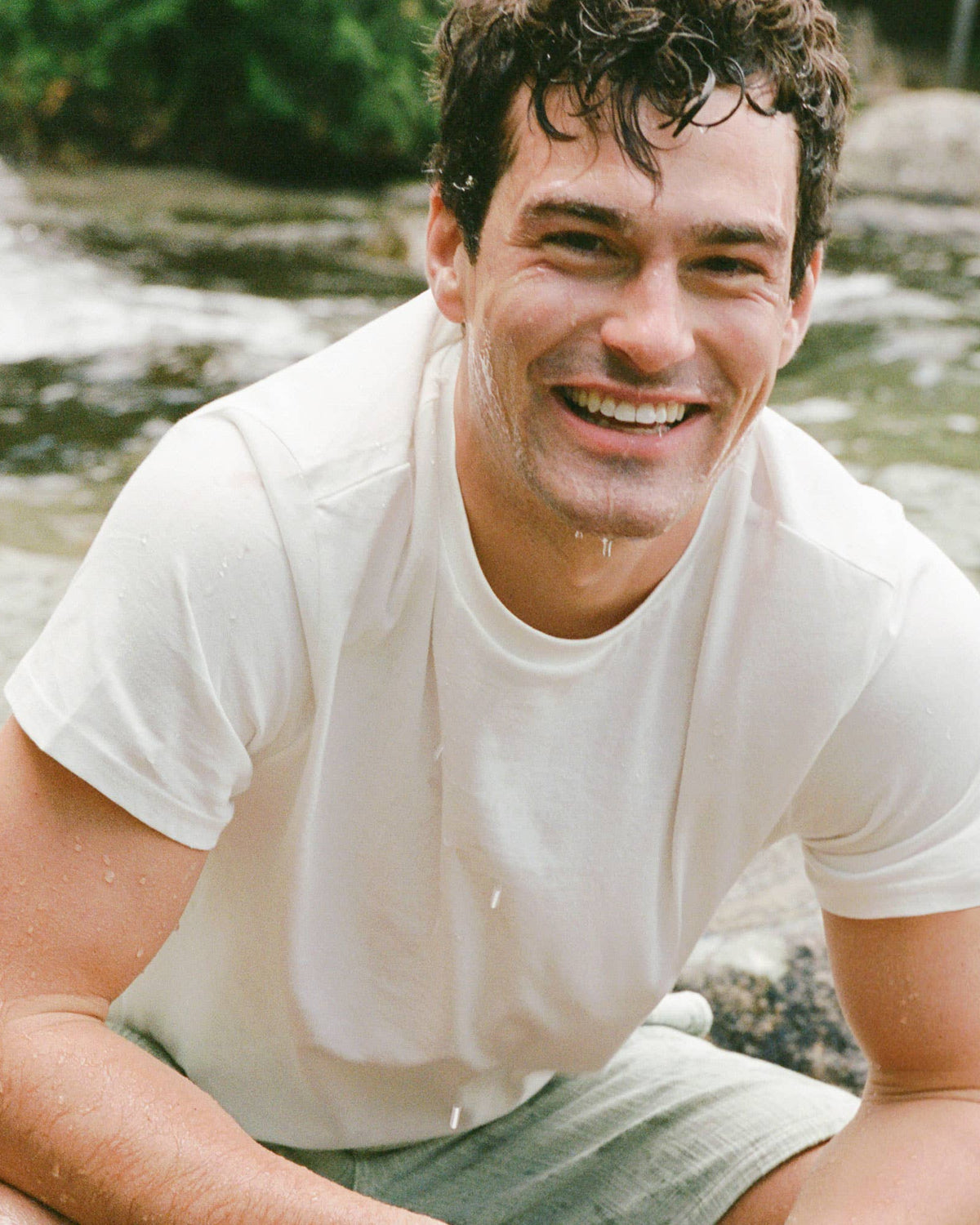 Man in a white t-shirt sitting by a stream with a natural background