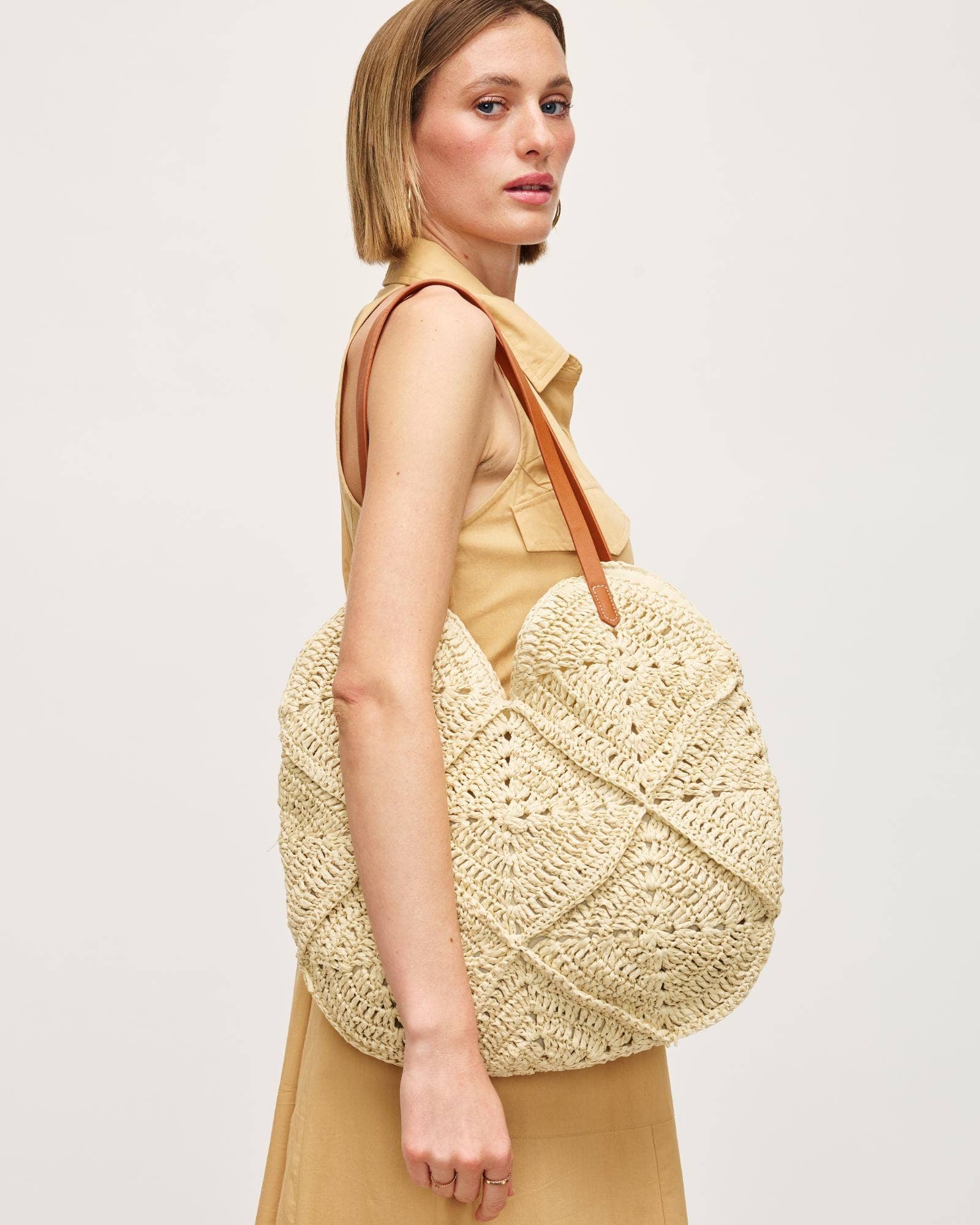 Woman holding a beige woven handbag against a plain background
