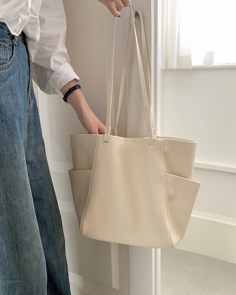 Person holding a beige tote bag in a minimalistic setting