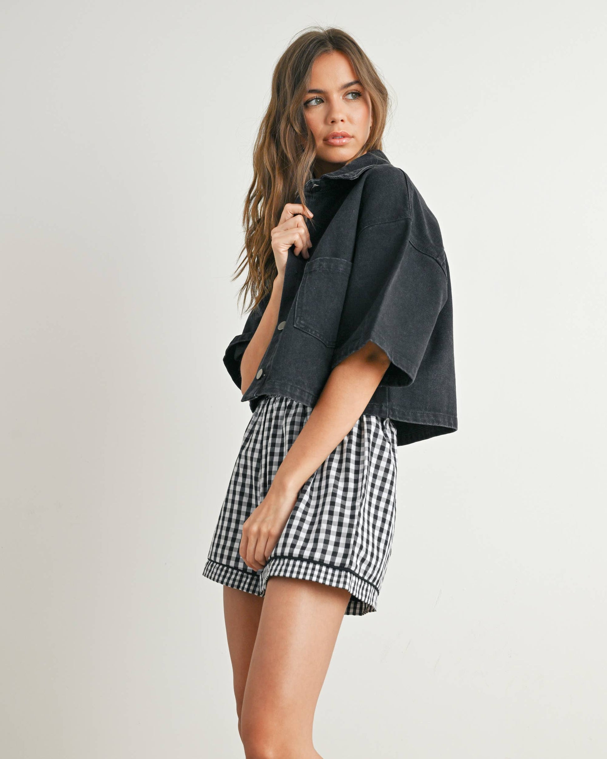 Woman wearing a dark jacket and checkered shorts on a plain background