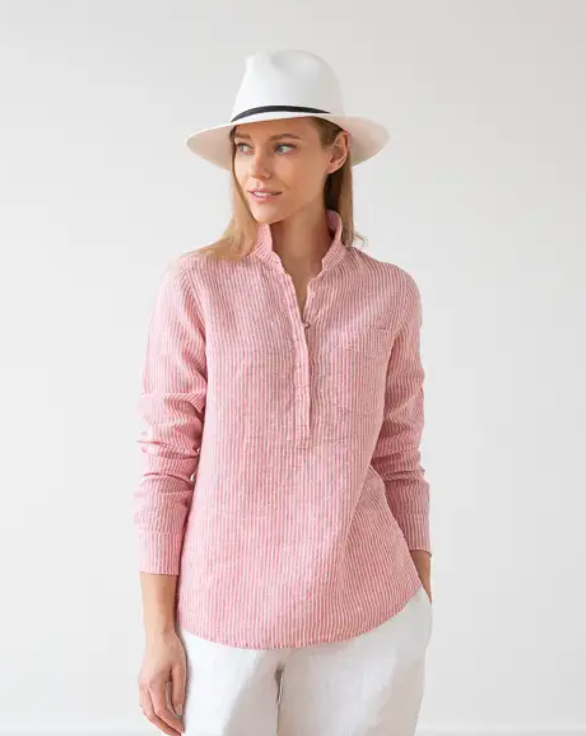 Model wearing LinenMe Stripe Fabio Shirt in Rose stripe wearing white pants and a white hat on a white background