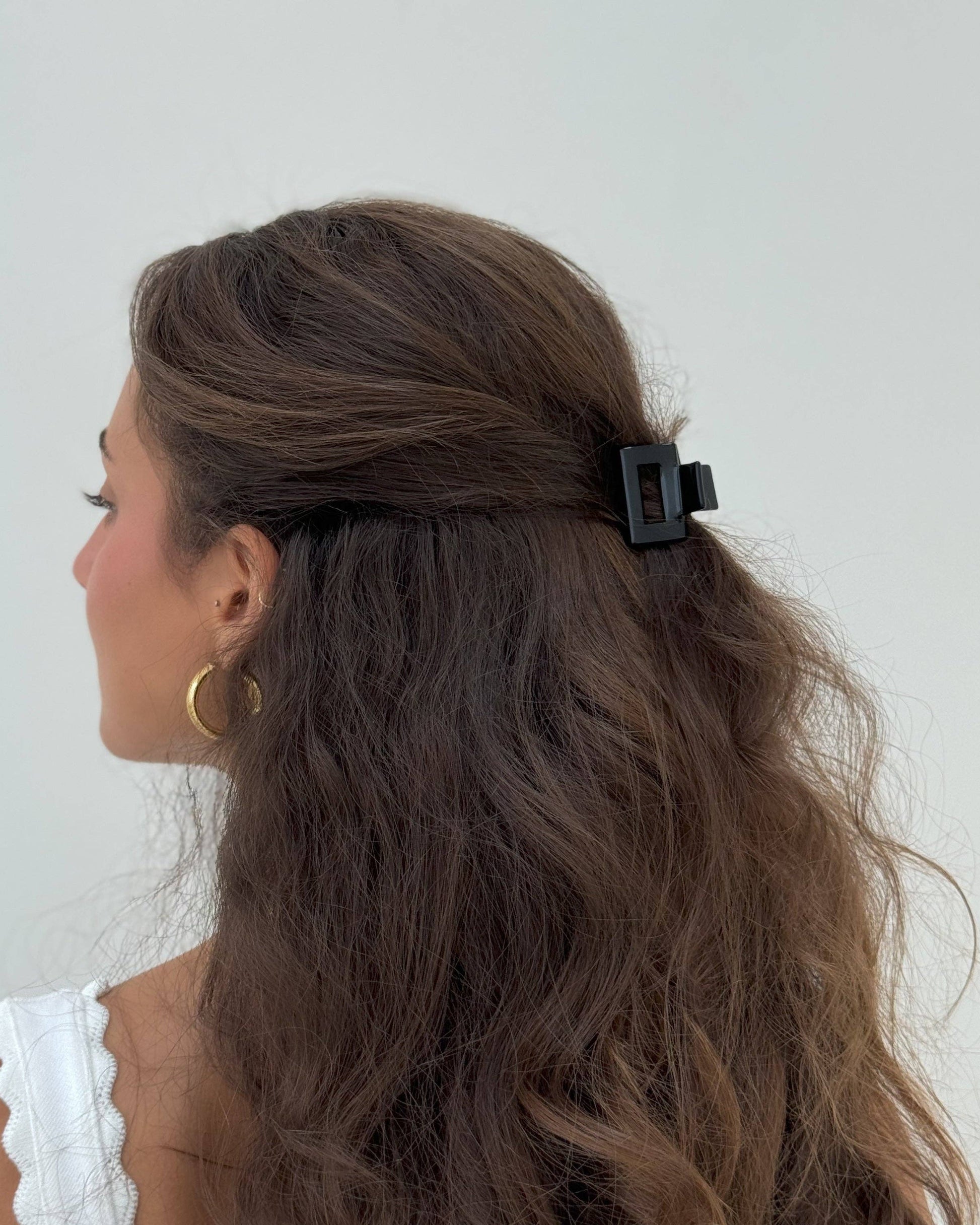 Woman with long brown hair tied back with a black clip against a white background