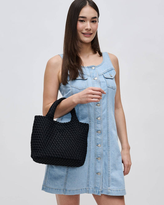 Woman holding a black woven handbag wearing a denim dress on a light gray background