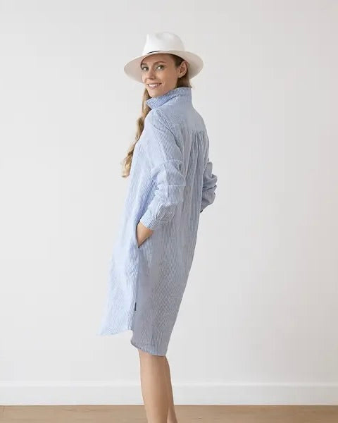 Side view of model wearing the LinenMe Linen Stripe Tee Dress in light blue with a white hat, standing against a white background