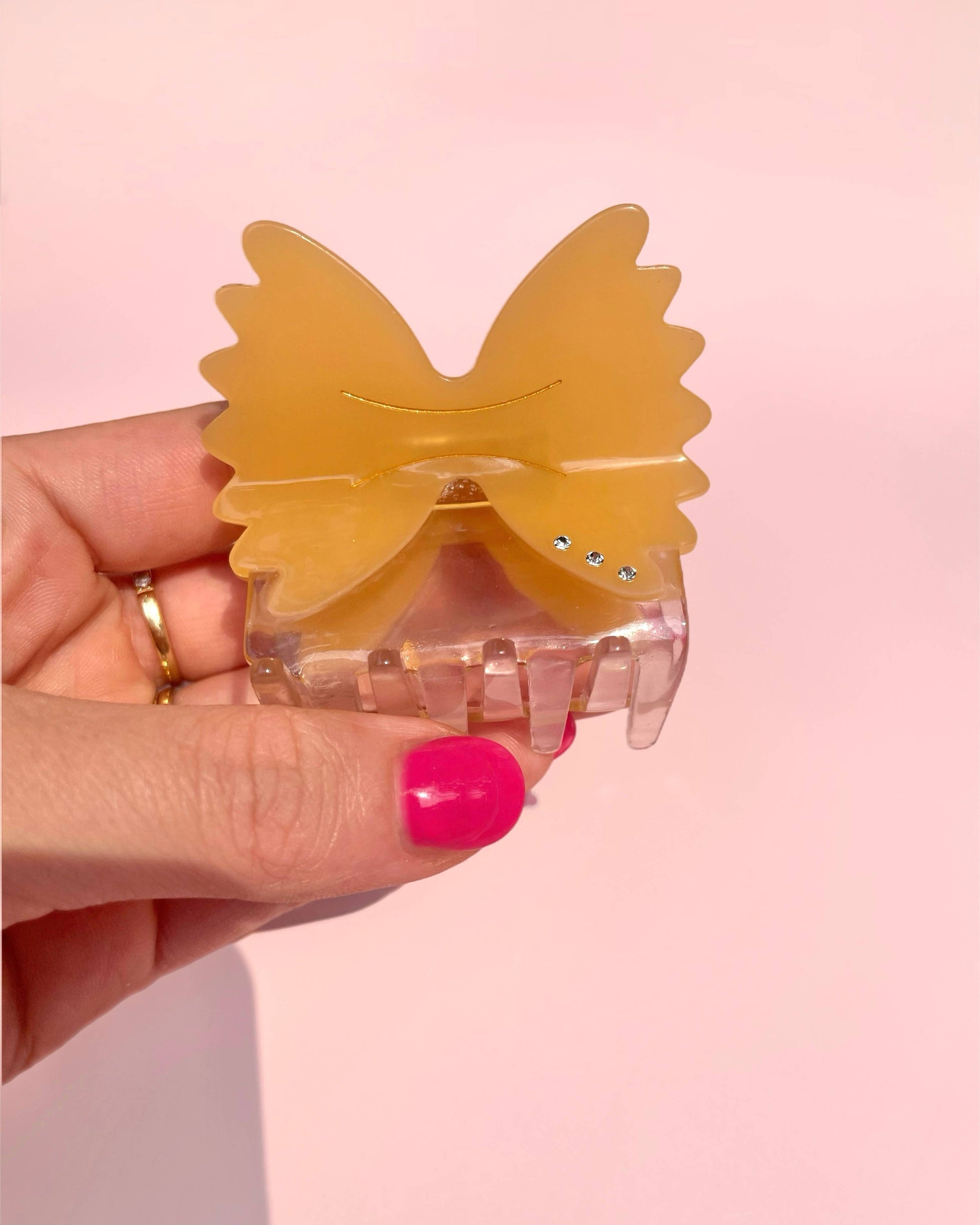 Hand holding a butterfly-shaped hair clip against a pink background