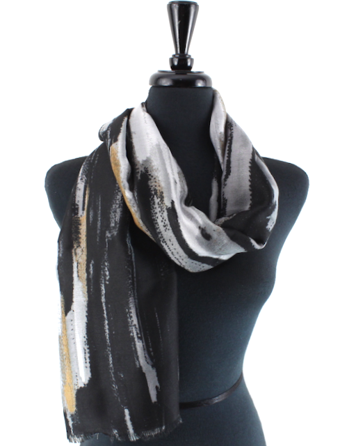 A lightweight scarf with an abstract black, white, and gold brushstroke pattern, draped on a black mannequin torso against a white background.