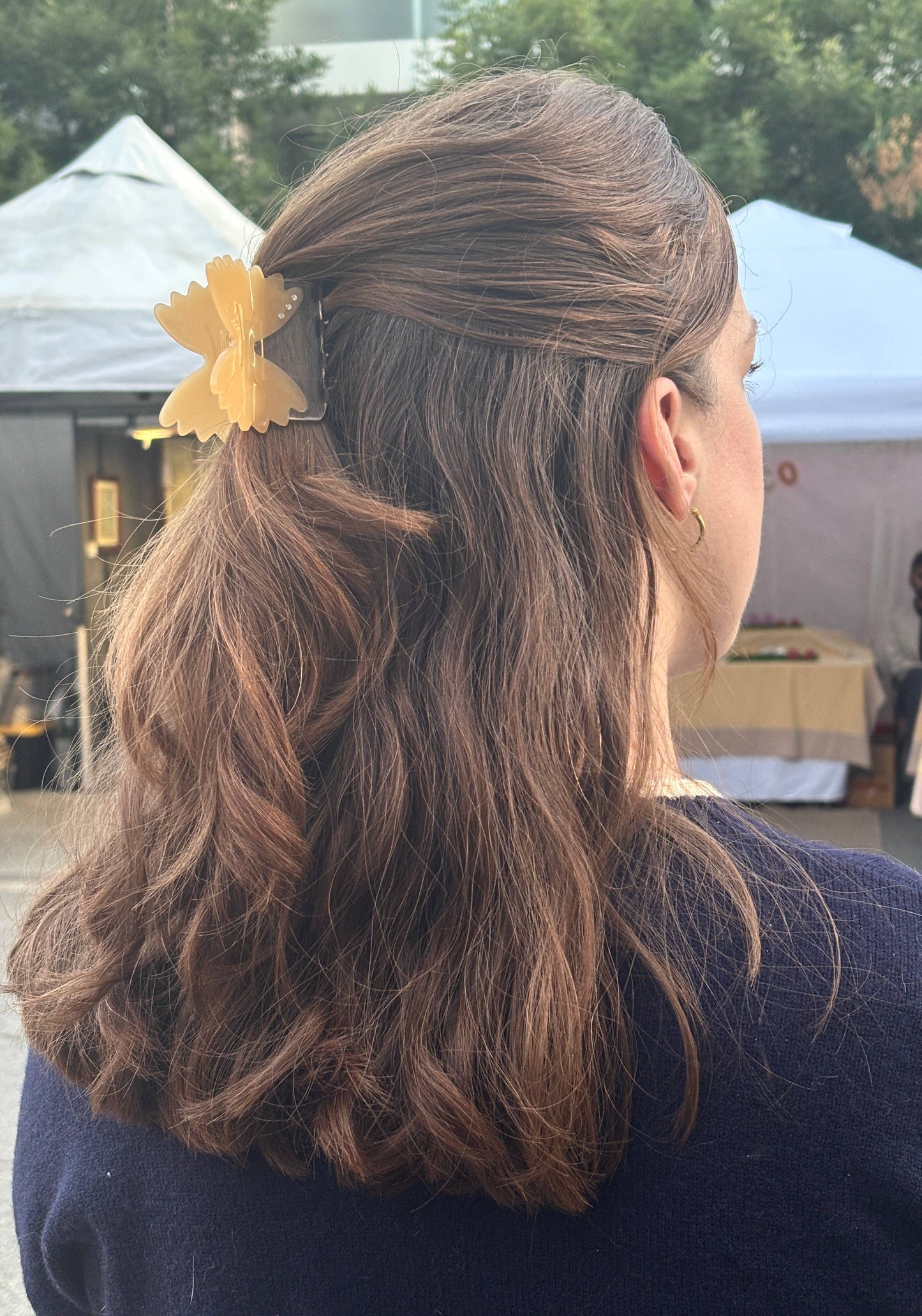 Person with wavy hair tied back with a yellow hair accessory, outdoors.