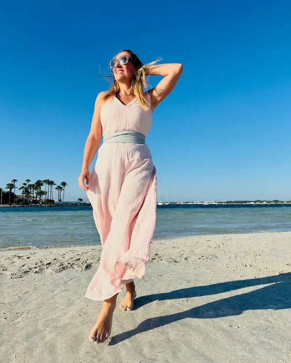 Woman in a pink dress standing on a beach with palm trees and water in the background