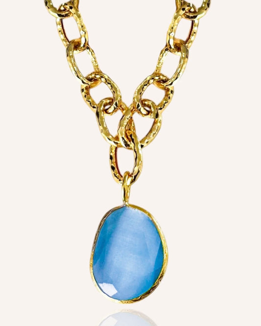 Gold chain necklace with a blue pendant on a white background