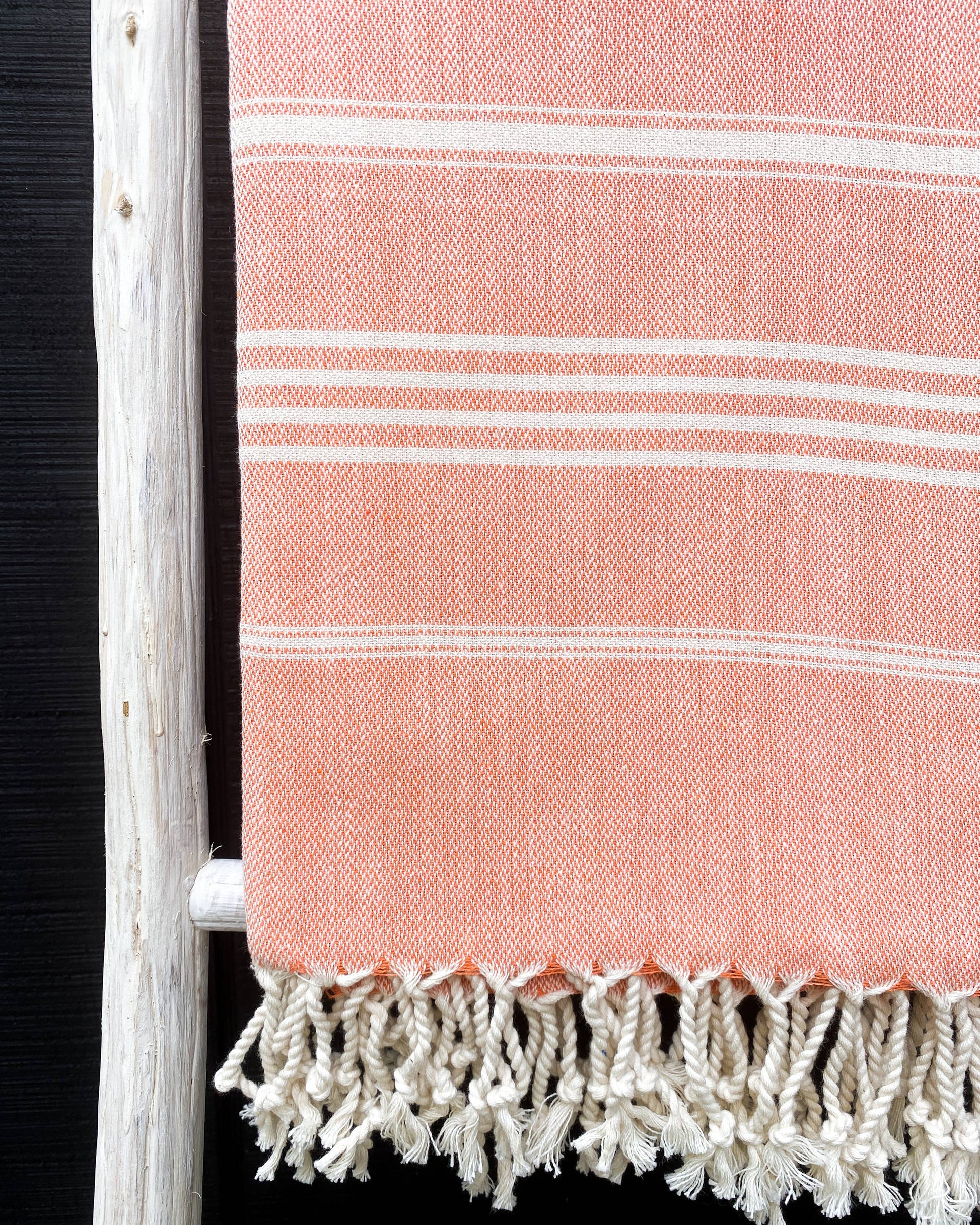 Pink towel with white stripes and frayed edge on a wooden ladder against a black background