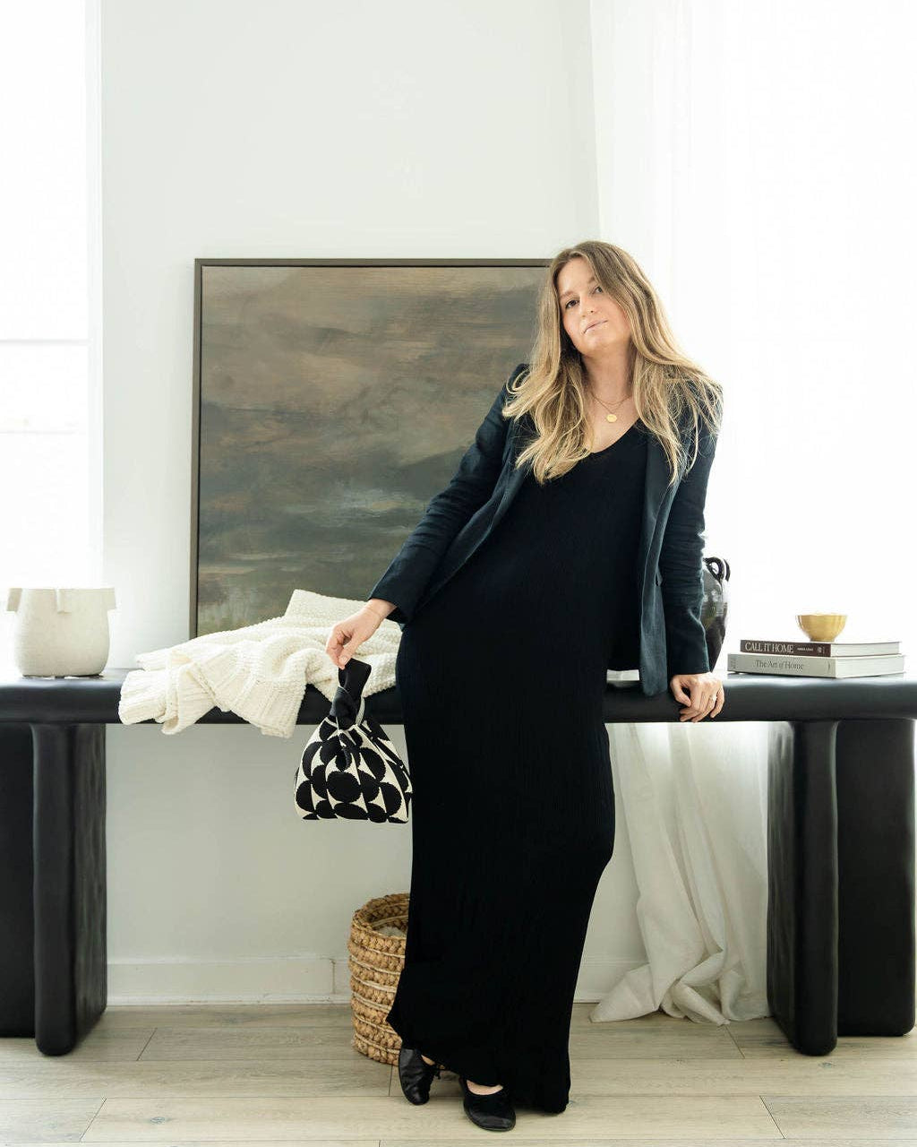 Woman in a black dress standing in a room with a large mirror and minimal decor.