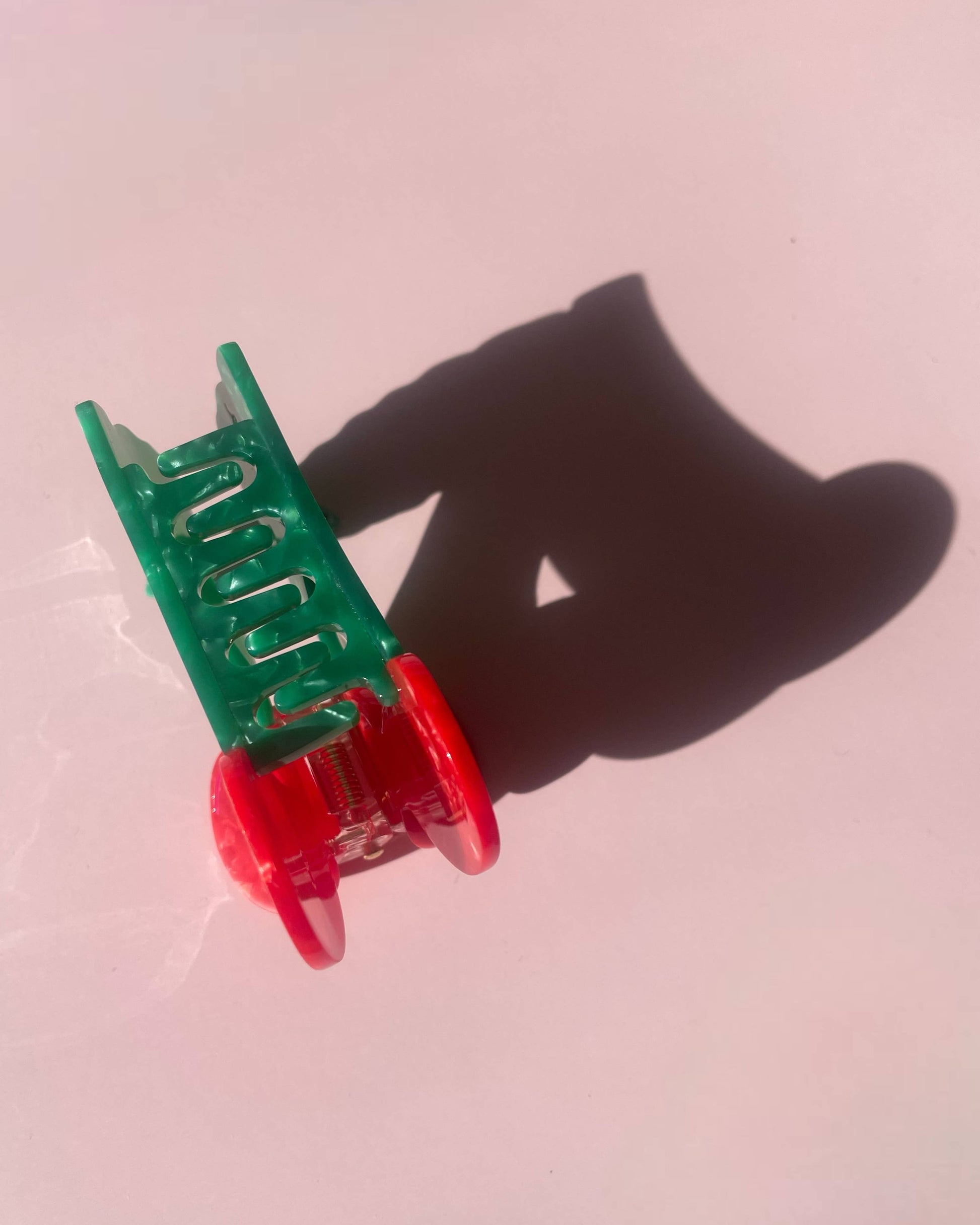 Front view of a cherry-shaped hair clip laying on a pink background