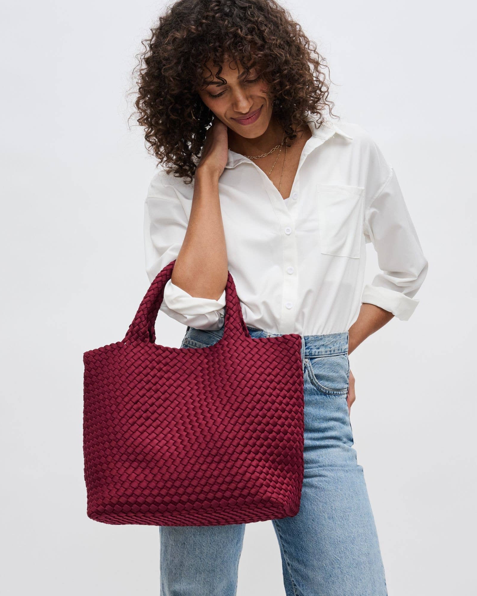 Woman holding a red woven handbag against a plain background