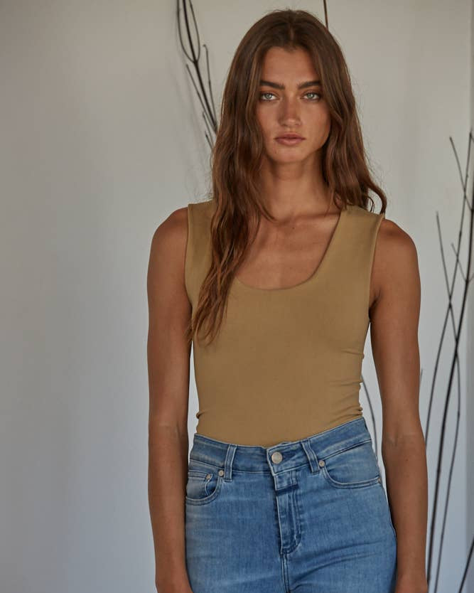 Woman wearing a beige tank top and blue jeans against a neutral background