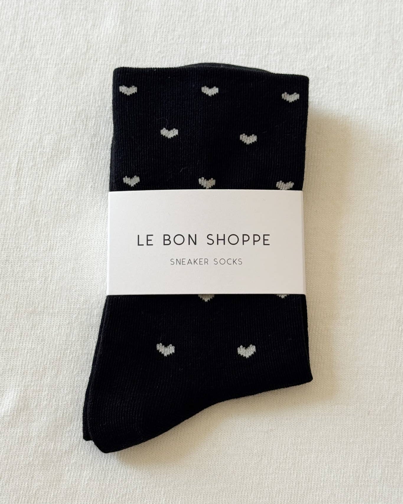 Black socks with heart patterns on a white background, labeled 'Le Bon Shoppe'.