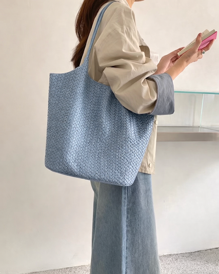 Person holding a blue textured tote bag in an indoor setting