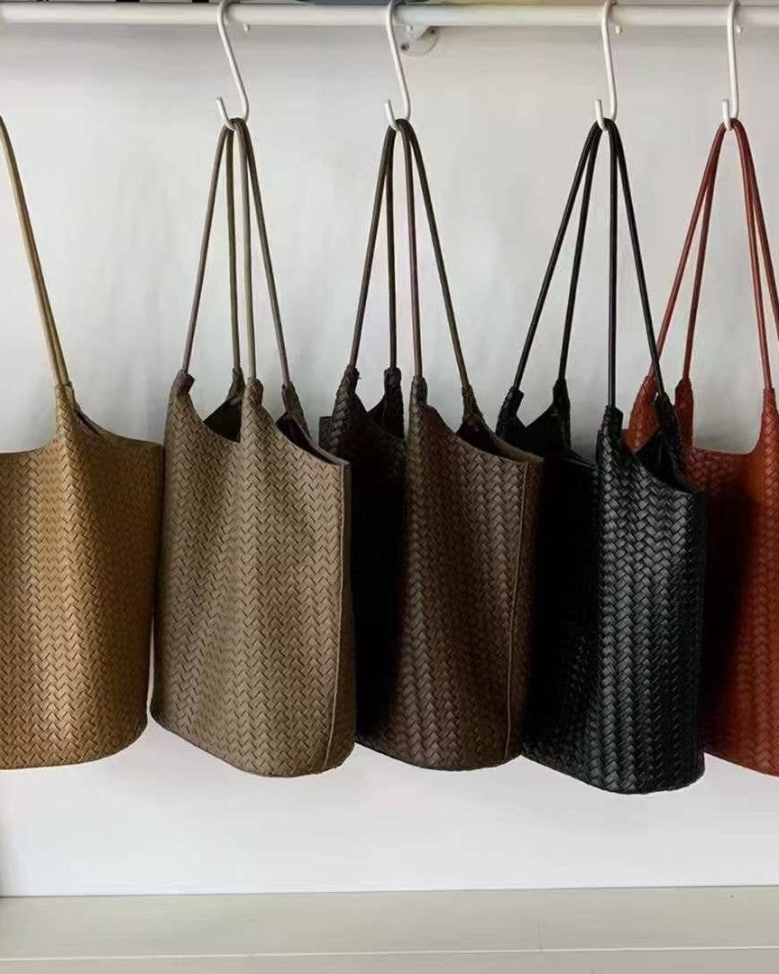 Five woven handbags in different colors hanging on a rack.