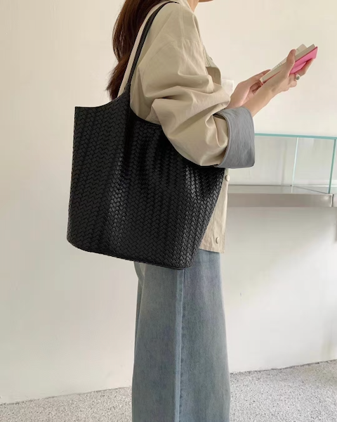 Person holding a black woven tote bag and a pink phone against a neutral background