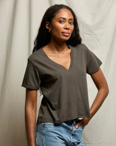 Woman wearing a dark green t-shirt and blue jeans against a neutral background