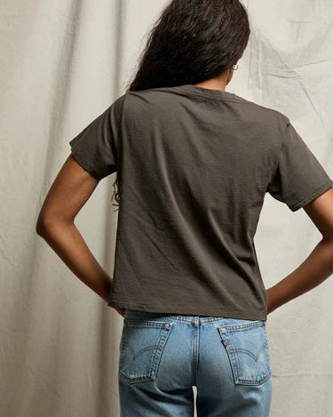 Person wearing a dark green t-shirt and blue jeans standing against a neutral background