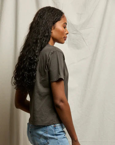 Woman wearing a dark gray t-shirt and light blue jeans against a plain background