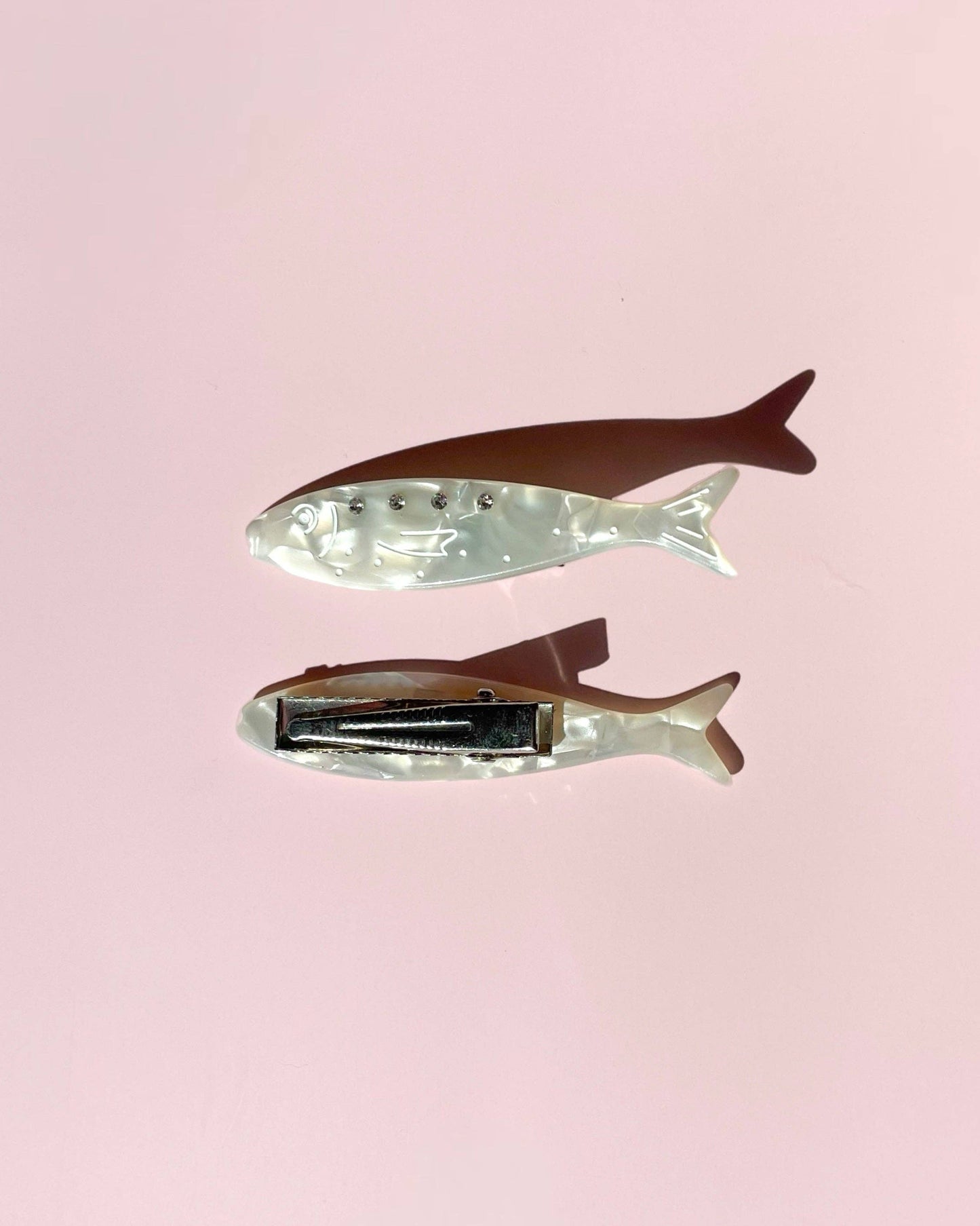 Two fish-shaped hair clips on a pink background