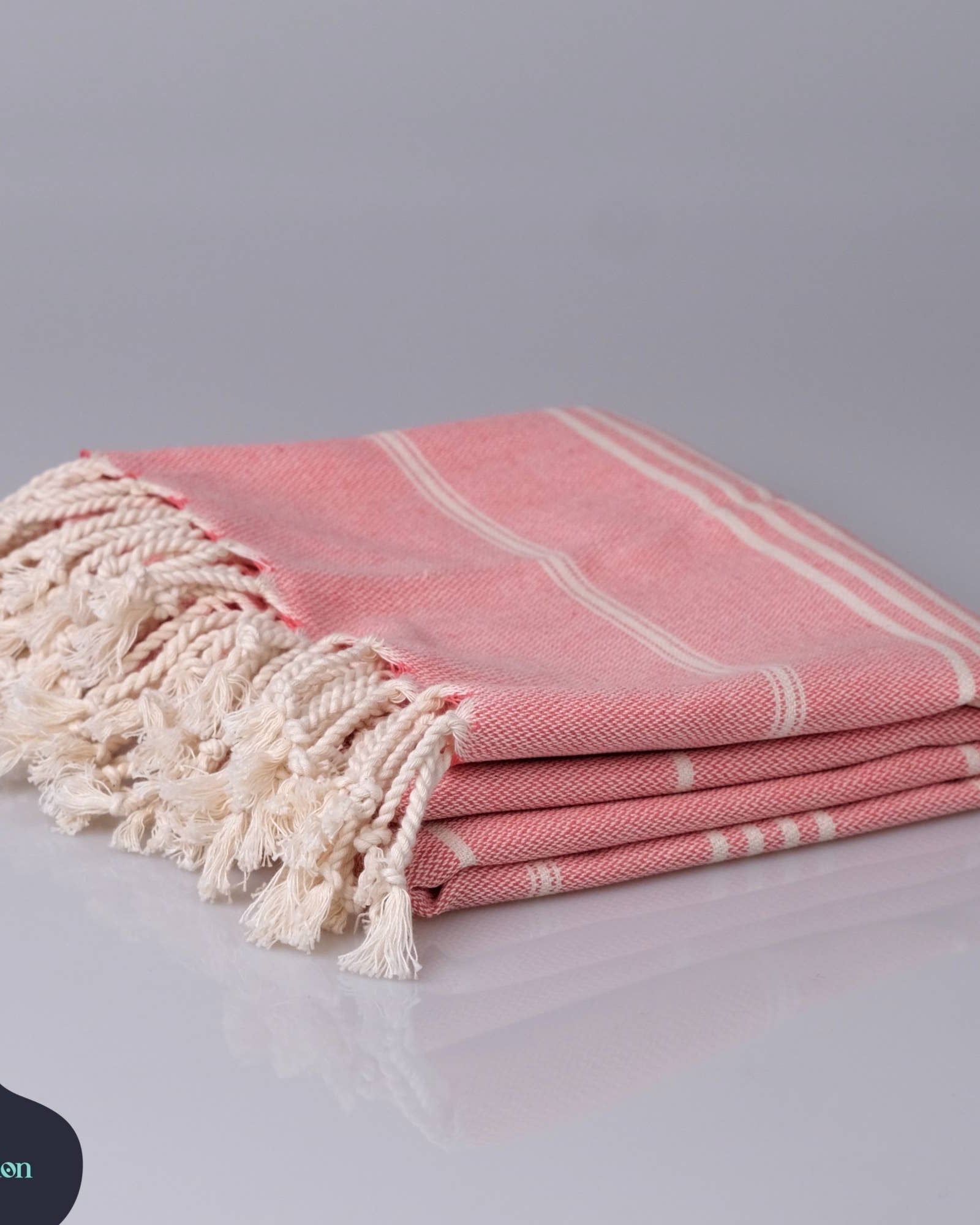 Pink towel with white tassels on a gray background