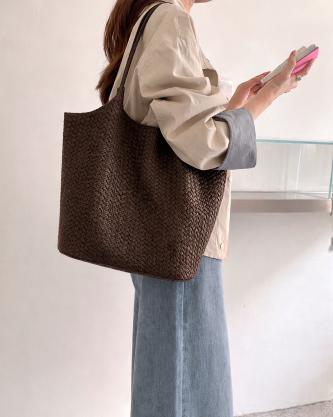 Person holding a woven brown tote bag and a phone against a plain background