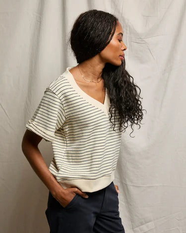 Woman wearing a striped shirt and dark pants against a neutral background