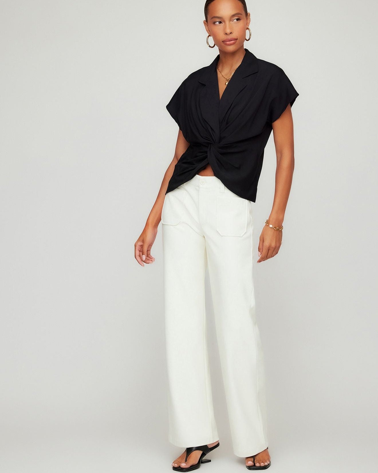 Woman wearing a black top and white pants on a plain background