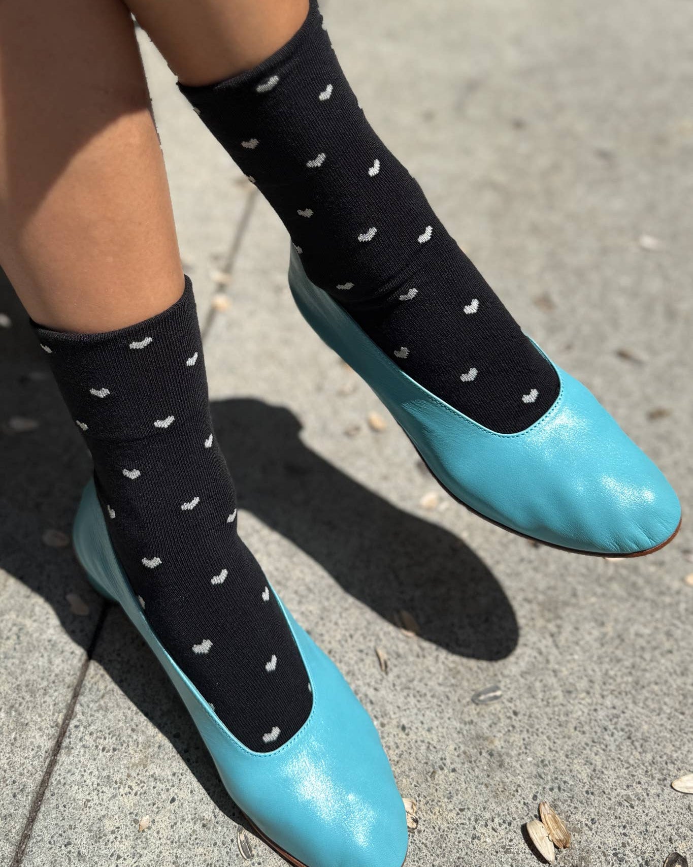 Person wearing black socks with white patterns and blue shoes on a concrete surface