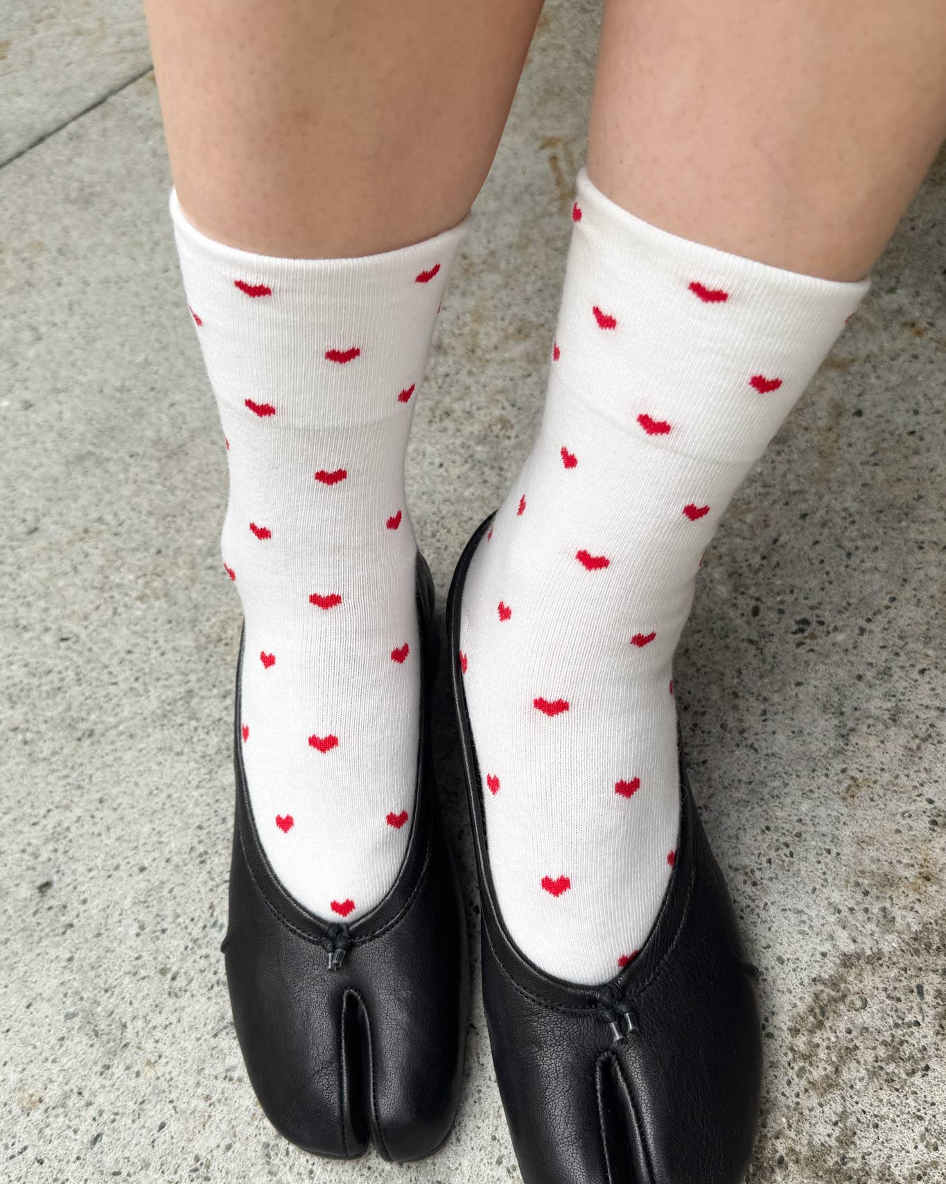 White socks with red heart patterns worn with black shoes on a concrete surface