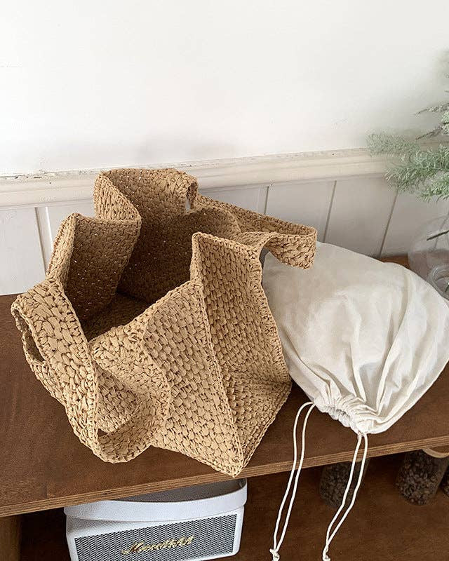 Two bags, one woven and one drawstring, on a wooden surface with a white background.